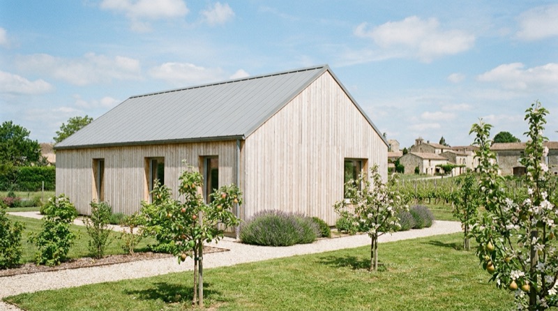 Maison modulaire en ossature bois à bardage clair dans un jardin de village